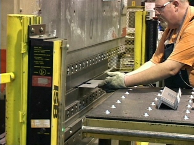 A worker following safe work practices to avoid injury while operating a machine to bend sheet metal
