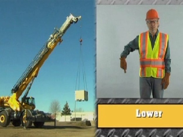 A crane signal person demonstrating the hand signal for a crane operator to safely lower their load