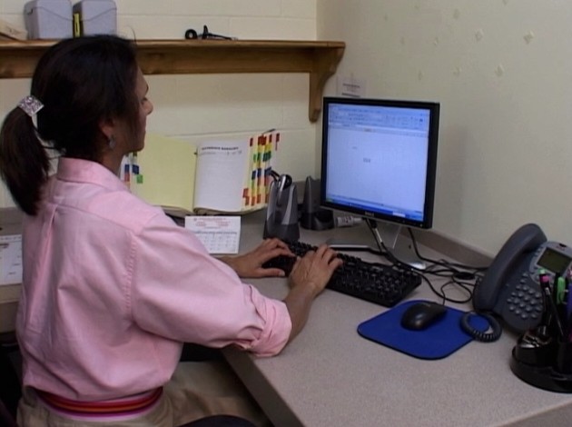 An office worker at her computer attempting to reduce the chance of an ergonomic related injury