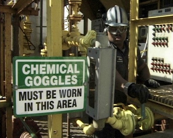 A PPE warning sign that chemical goggles must be worn in this area and a worker wearing proper PPE