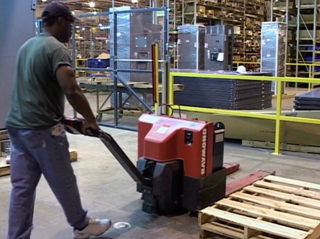 A warehouse worker safely operating an electric pallet jack to avoid injury in the workplace