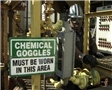 A PPE warning sign that chemical goggles must be worn in this area and a worker wearing proper PPE